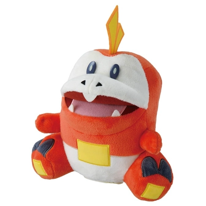 Fuecoco plush toy with open mouth, orange body, white accents, and a yellow flame on its head.