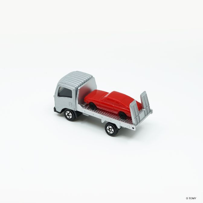  Silver toy truck carrying a red toy car on its flatbed.