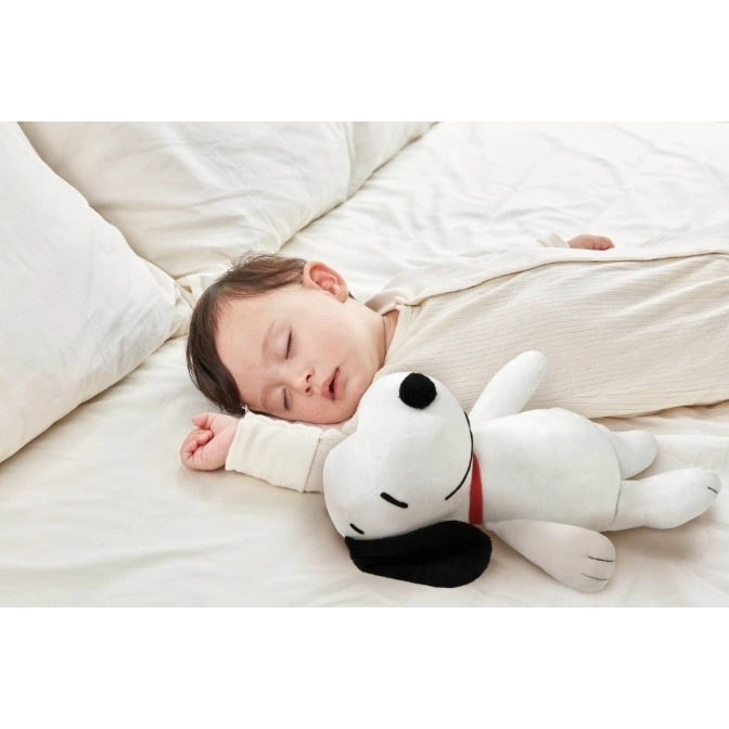 Baby sleeping with a Snoopy plush toy on a white bed.