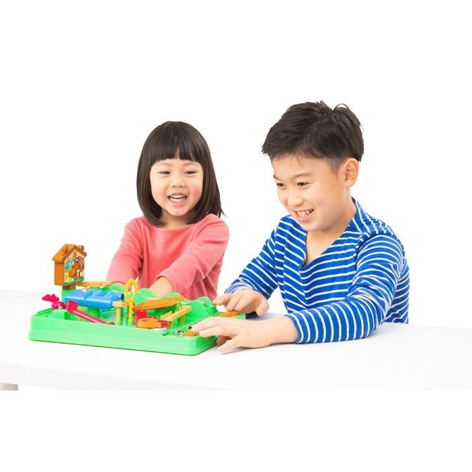  Children playing the Mouse Trap game, a chain reaction contraption with a house and various obstacles on a green base.
