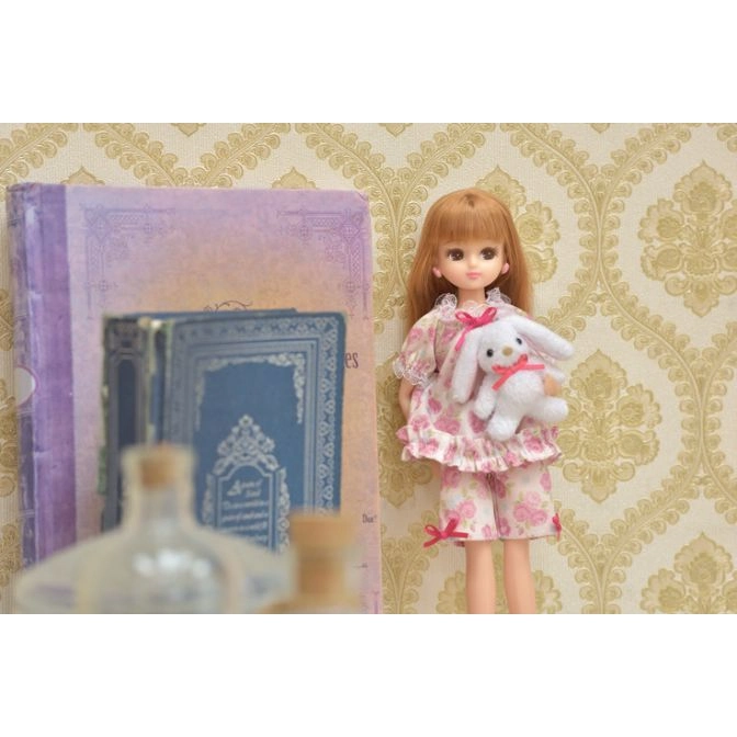  Doll in floral pajamas holds a plush bunny with a pink bow, next to books.