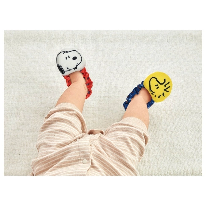  Baby wearing Snoopy and Woodstock wrist rattles, lying on a blanket.