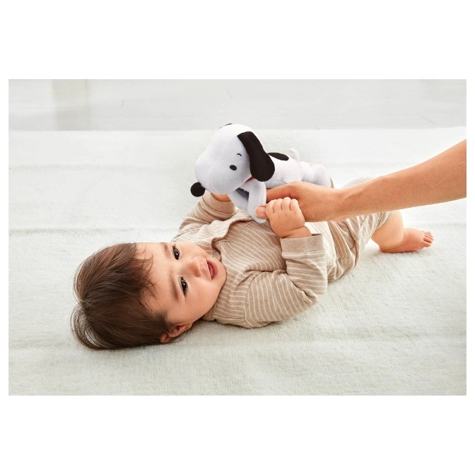  Baby lying down playing with a Snoopy plush toy held by an adult hand.