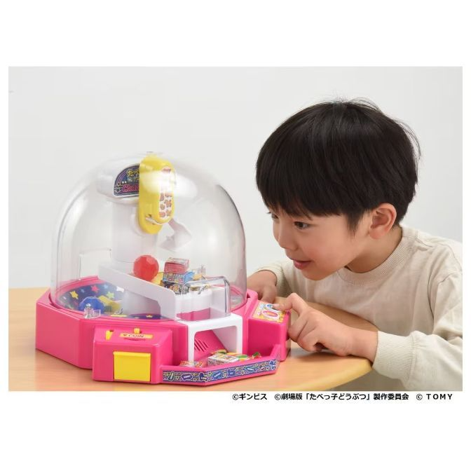 Boy playing with a pink UFO catcher toy with a clear dome and a red ball inside.