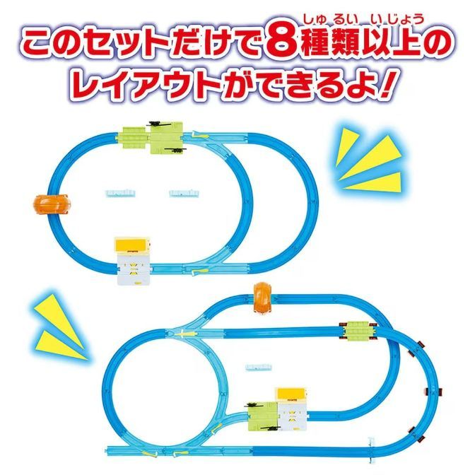  Two different layouts of a blue toy train track are displayed. The top layout features a figure-eight shape with a green and yellow train station and an orange train. The bottom layout also has a figure-eight shape but with a different configuration of the track and train station.
