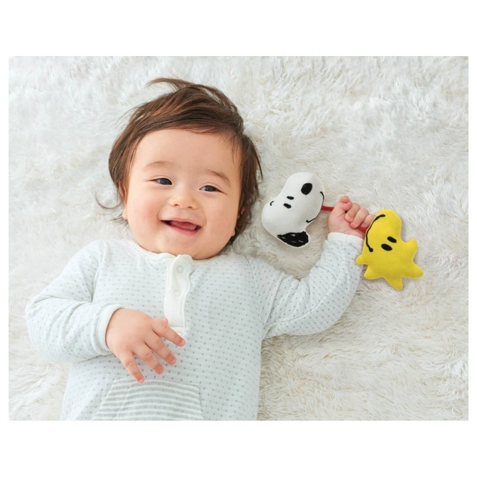  Baby lying on a rug holding a Snoopy and Woodstock rattle toy.