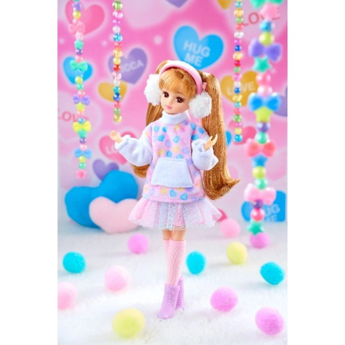  Licca-chan doll in a pastel outfit with earmuffs, standing amidst colorful pom-poms and beaded garlands.