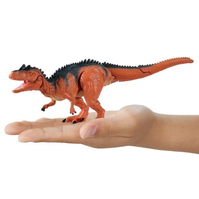  Orange dinosaur toy with black spikes being held in a hand.