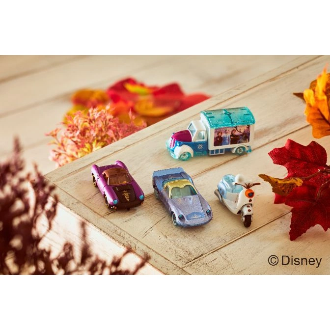  Disney Frozen diecast toy vehicles including a truck, two cars, and a scooter on a wooden surface with fall foliage.