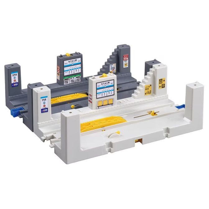  A toy train station set with two platforms, one gray and one white, featuring stairs, signs, and yellow accents.