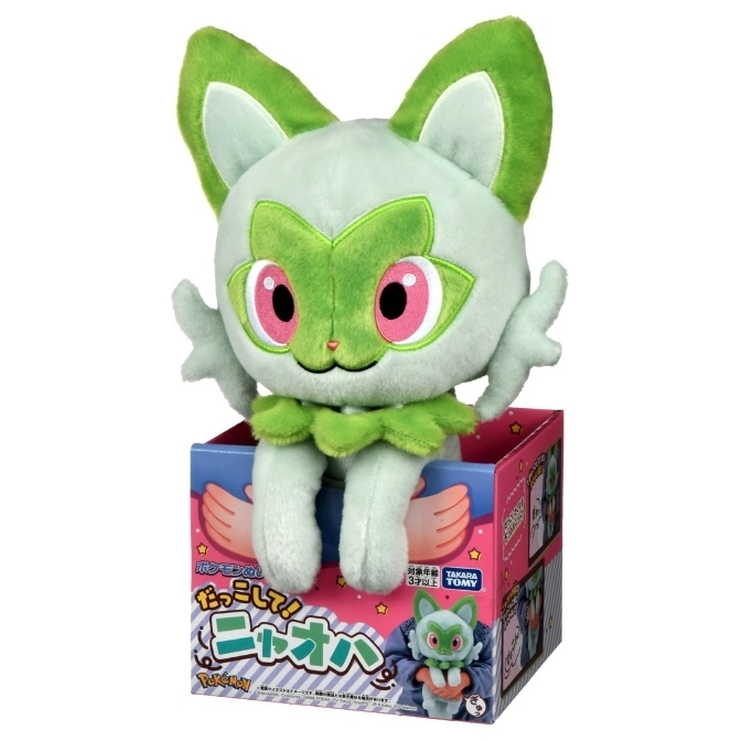 Sprigatito plush toy in box. Green and white cat-like Pokémon with pink eyes.