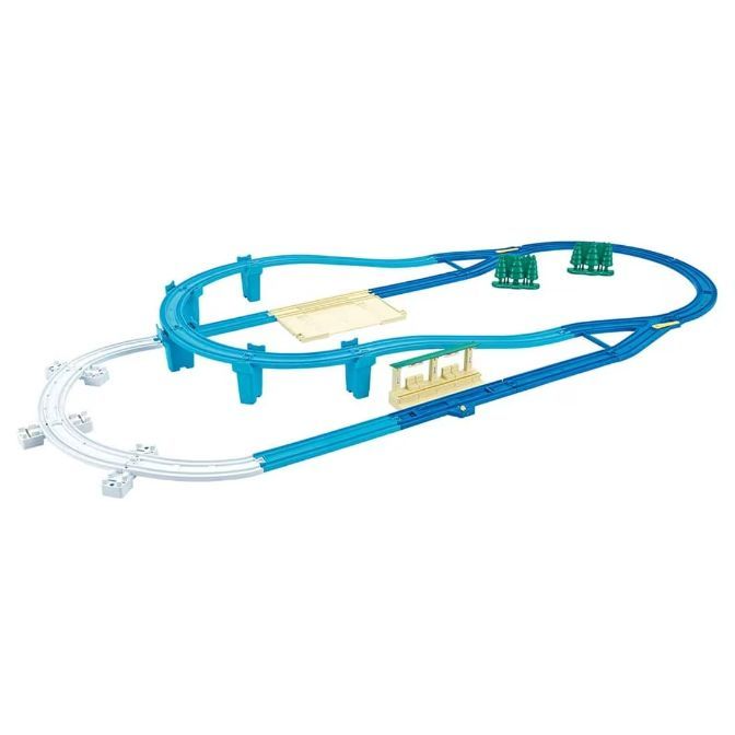 A toy train track set with blue and white tracks, a bridge, and green trees.