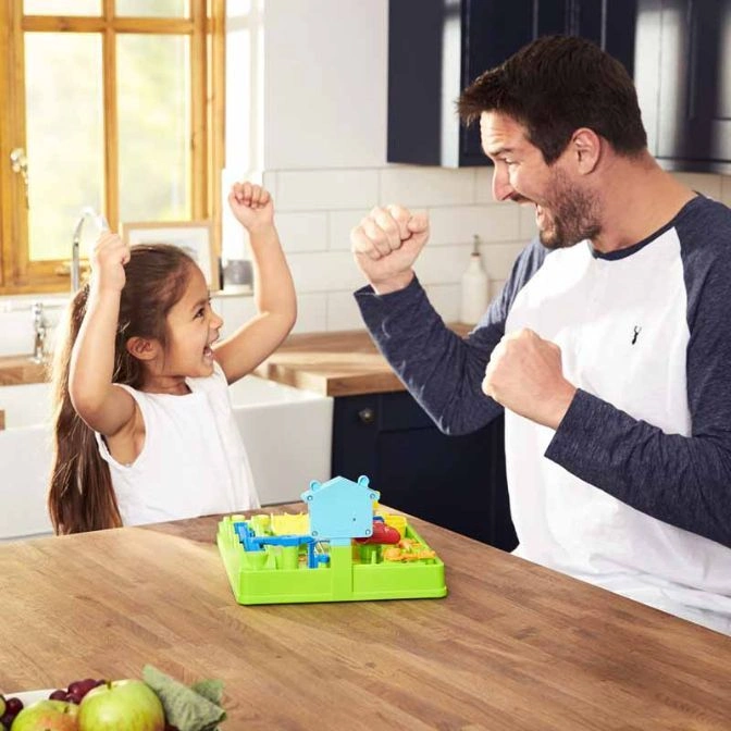  A father and daughter celebrate playing a green and blue board game on a wooden table.