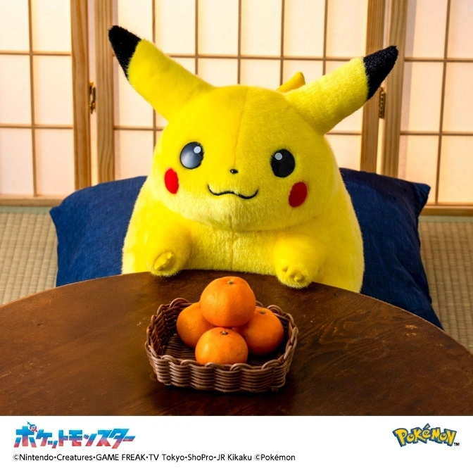 Pikachu plush with oranges on a table, seated on a blue cushion in front of a shoji screen.