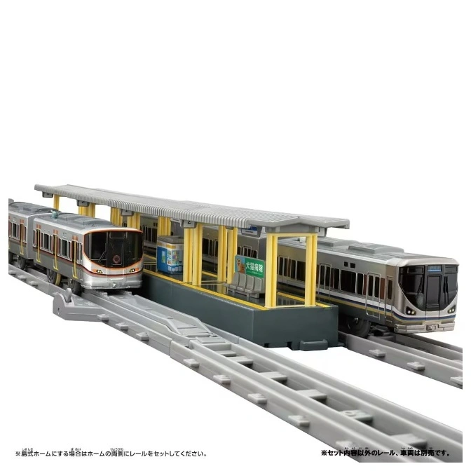  Toy train station with two model trains on tracks, featuring a platform and overhead shelter.