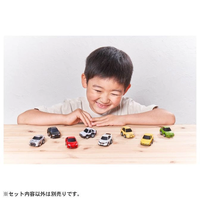  Smiling boy with toy cars on a wooden table. Variety of colors and models.