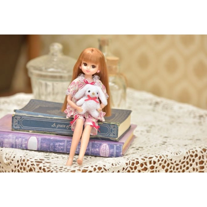  Doll in floral pajamas holding a plush bunny while sitting on stacked books.