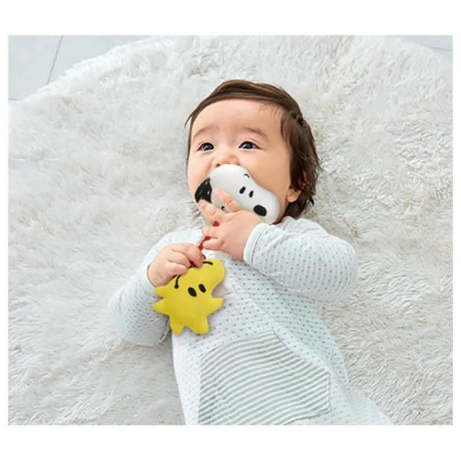 Baby lying on a rug chewing on a Snoopy teether toy with a yellow Woodstock plush.