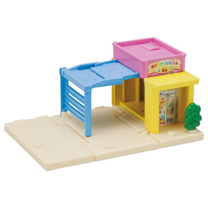  Toy playset with a blue slide, pink roof, yellow building, and a small green tree.