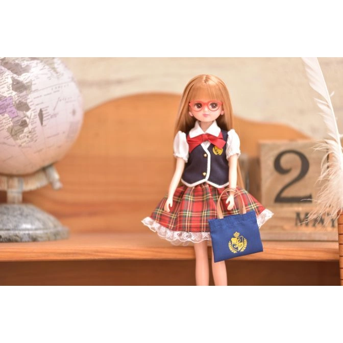  Fashion doll in school uniform with glasses and a tote bag, standing on a wooden surface.