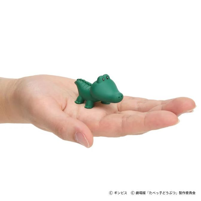 Green toy crocodile on a hand. Small, cartoonish design.