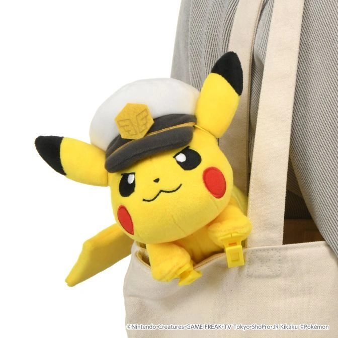  Pikachu plush toy wearing a captain's hat, peeking out of a tote bag pocket.